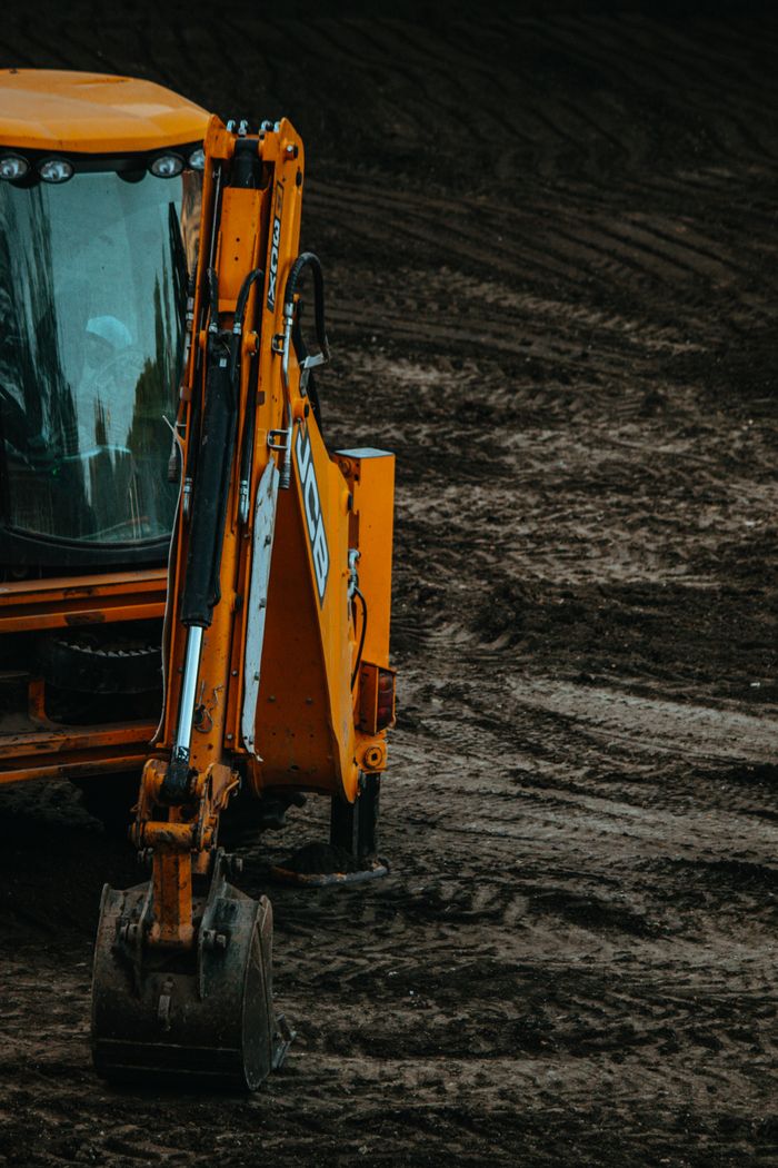gallery-5 Close-up of a yellow excavator on a construction site with muddy terrain.