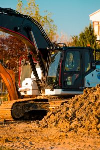 Excavator at a construction site with dirt piles and trees in background.