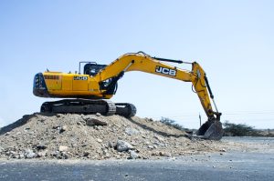 Yellow excavator on a pile of dirt at a construction site under clear blue sky.