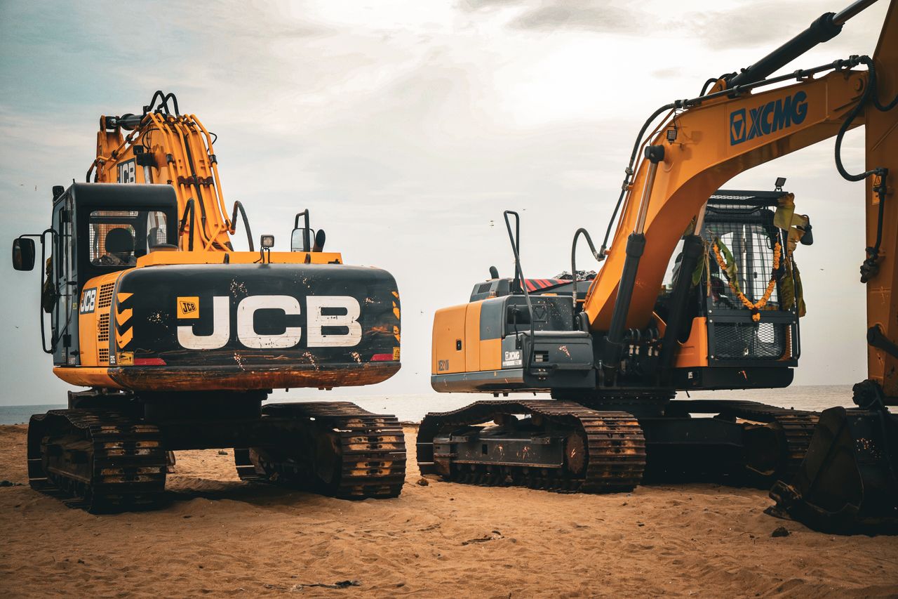 services-01 Two heavy excavators on a sandy beach, showcasing industrial construction machinery.
