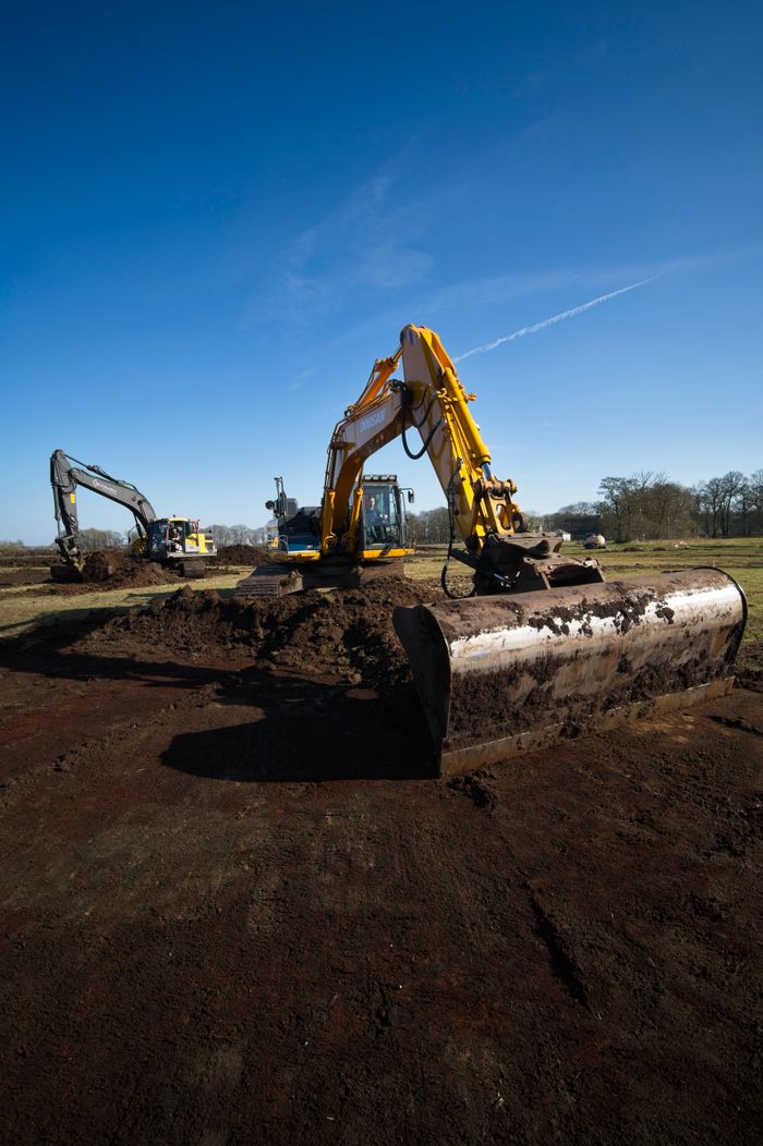 ours-journey Excavators operating in an open field under a clear blue sky.