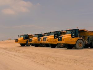 Row of heavy-duty dump trucks parked on a sandy construction site under a clear sky.