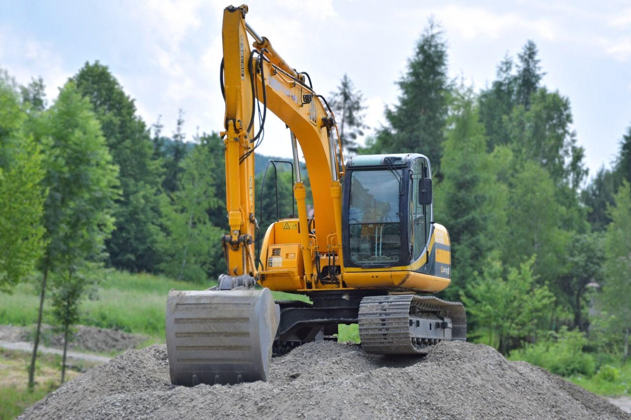 gallery-6 A yellow excavator on a pile of gravel in a lush, green forest setting in Poland.